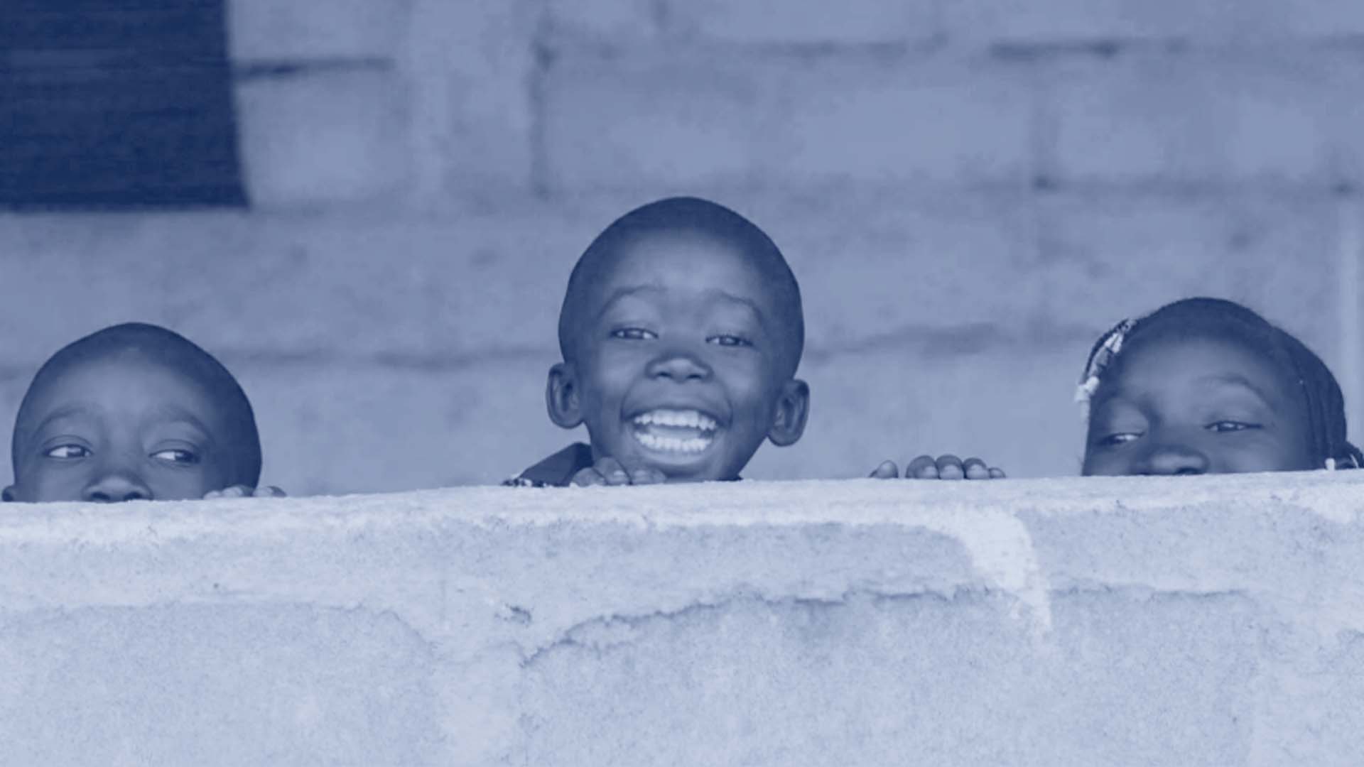three children peeking over a wall smiling