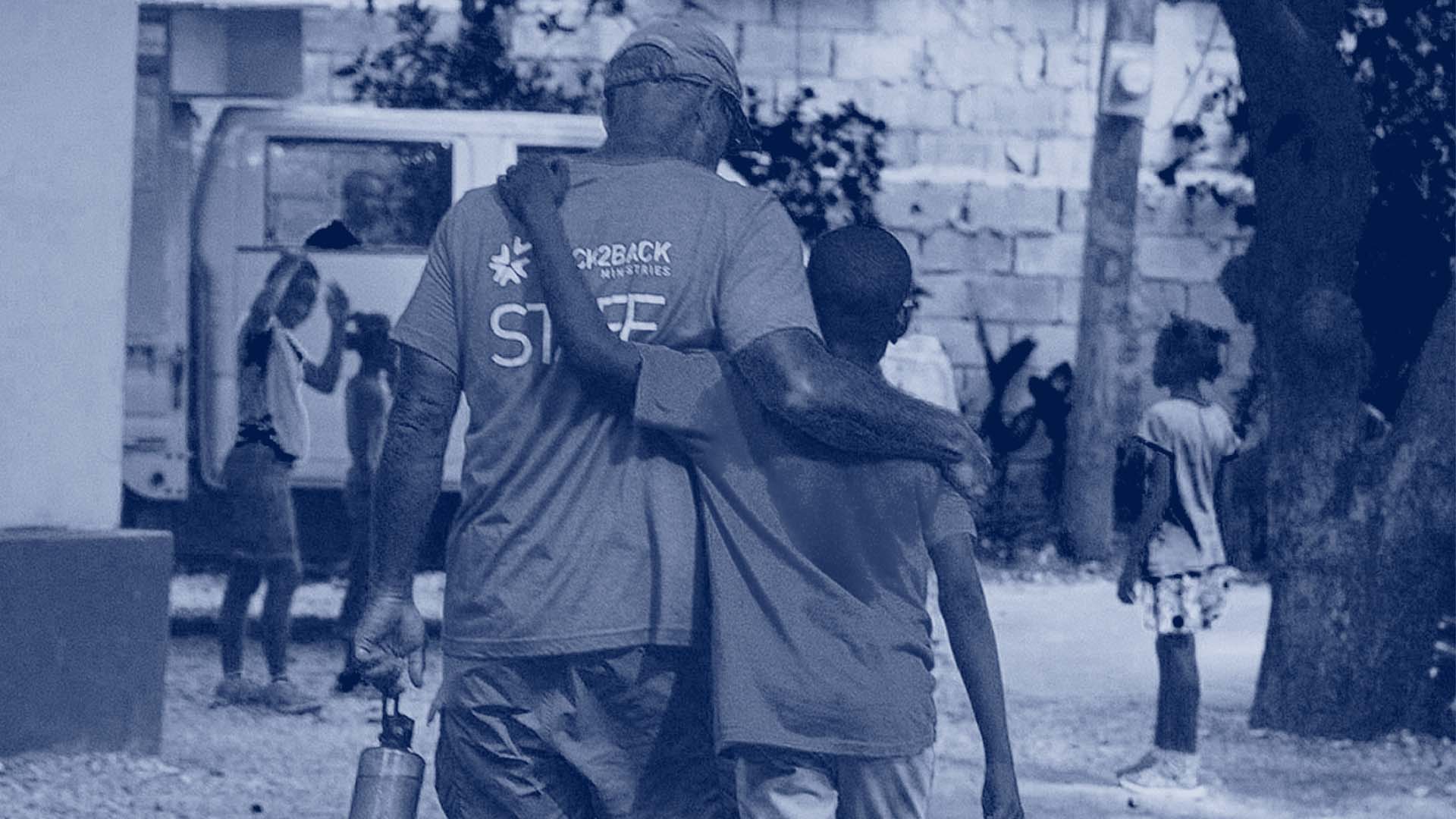 A man and a boy walking down the street with their arm around each other.